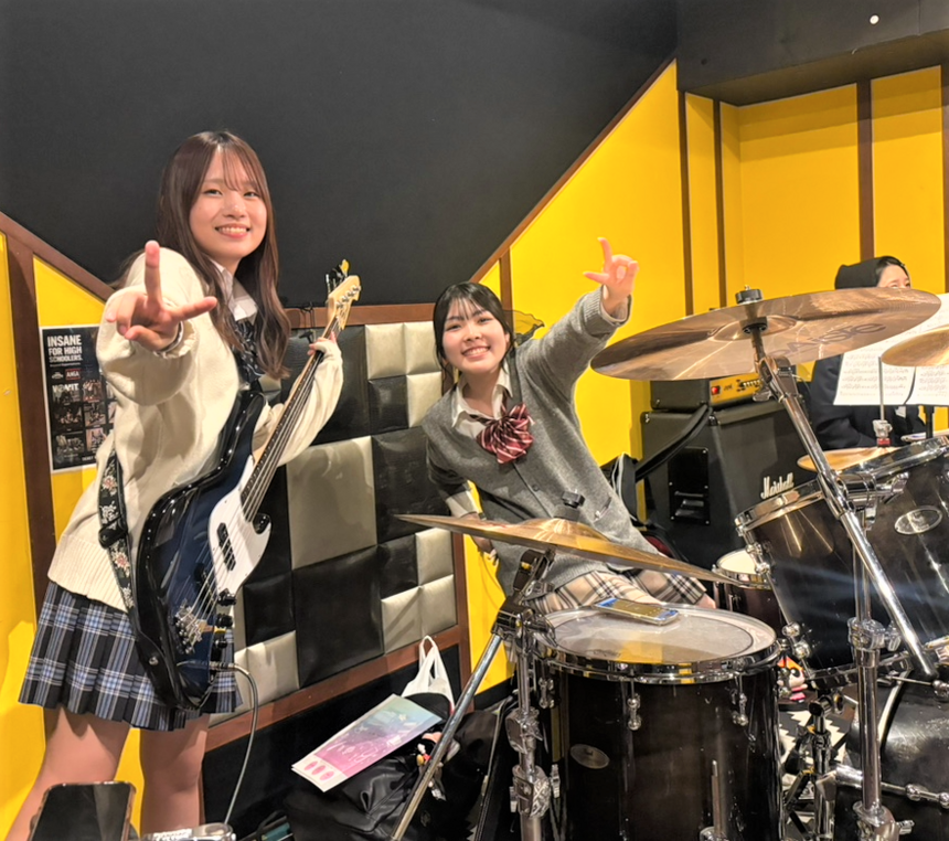 楽器に囲まれた女子2名がポーズを取っている様子