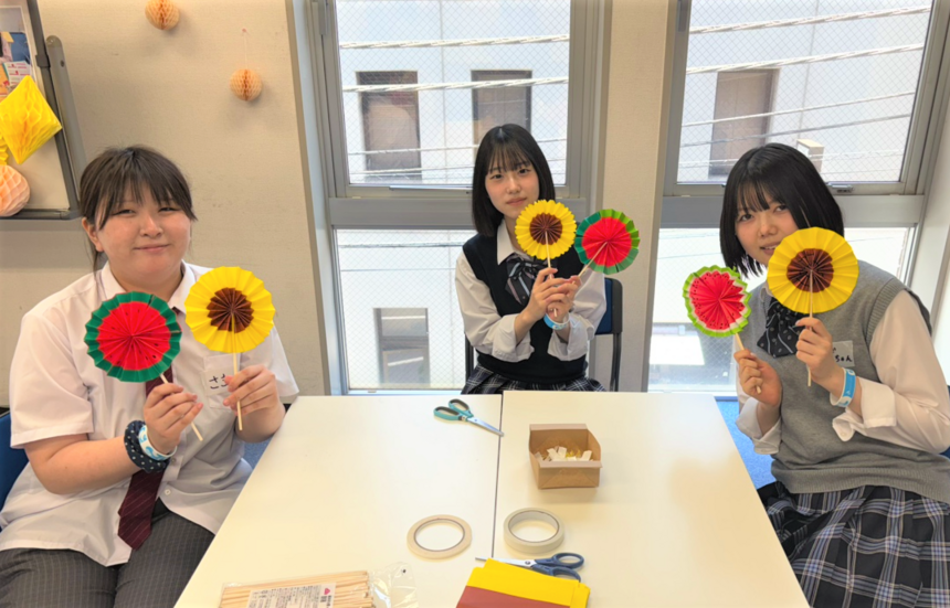 女子高校生3人がスイカやヒマワリの団扇を持っている様子