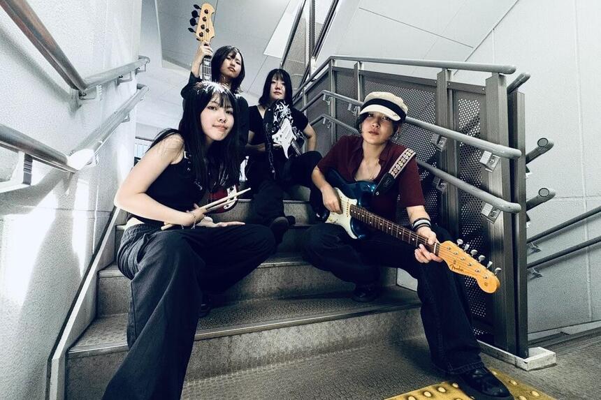女子高校生4人組のバンドチームが楽器と共にポーズを取っている様子