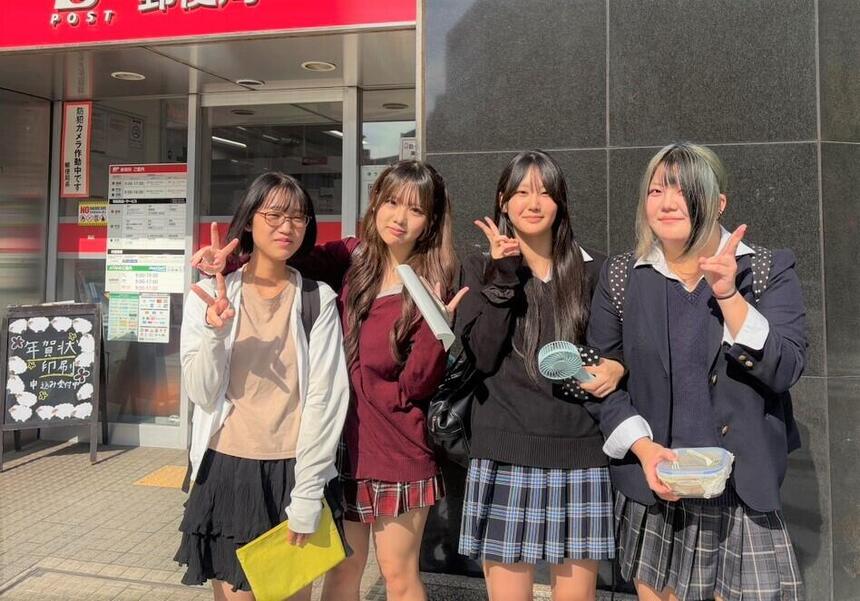 女子高校生4名で銀行前でポーズを取っている様子