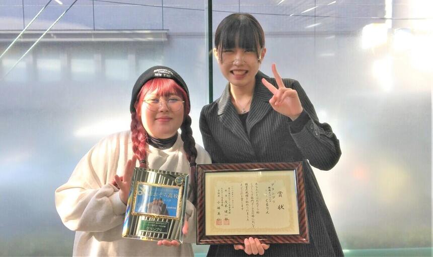 右に賞状を持つ生徒。左に盾を持つ生徒。笑顔でピースサインをしている。
