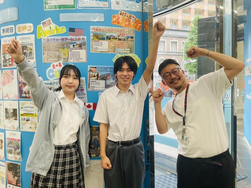 7月1日の国内留学プログラムに参加前の生徒の様子です。場所は福岡キャンパスの入り口で、2年次の二人がそれぞれが国内留学に向けて英語の準備を進めています。