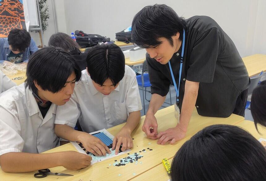 生徒が、切符アートの下絵に、1センチ角に切った使用済み切符を丁寧に貼っています。
