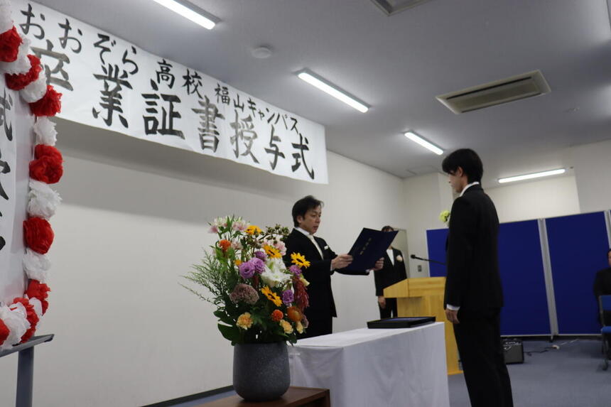 福山キャンパス1階での卒業式で、卒業生がキャンパス長から卒業証書を受け取る様子