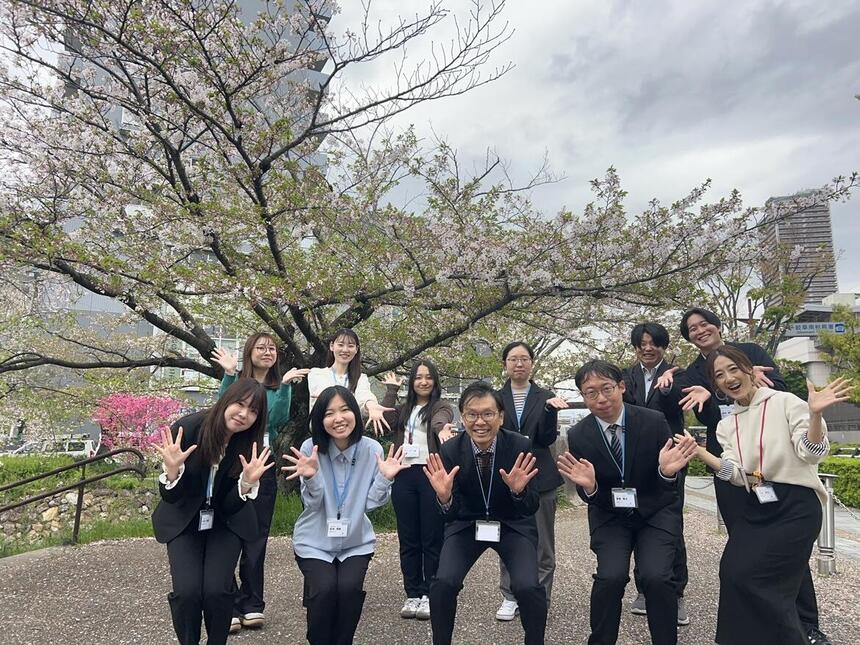 桜の木の下で岐阜キャンパスのコーチ11人が笑顔で手を振っている写真