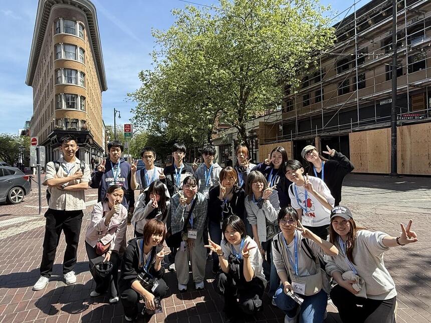 ビルの前で、みんながピースをしている集合写真