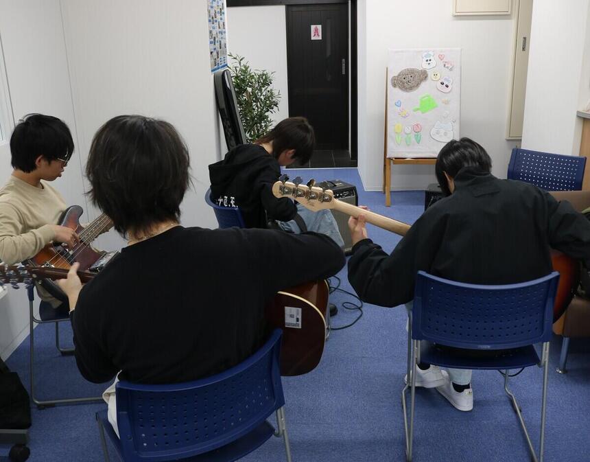 教室で、4人の生徒がベースとアコギを練習している様子