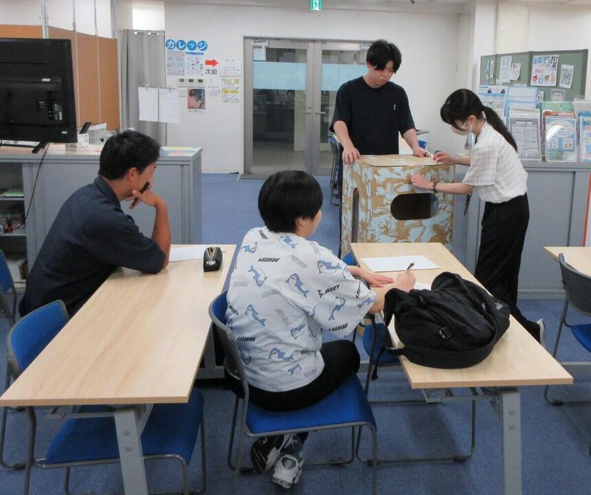 生徒3人、コーチ1人が教室でみらかけの時間に古着回収BOXのデザインをどうするか考えている様子
