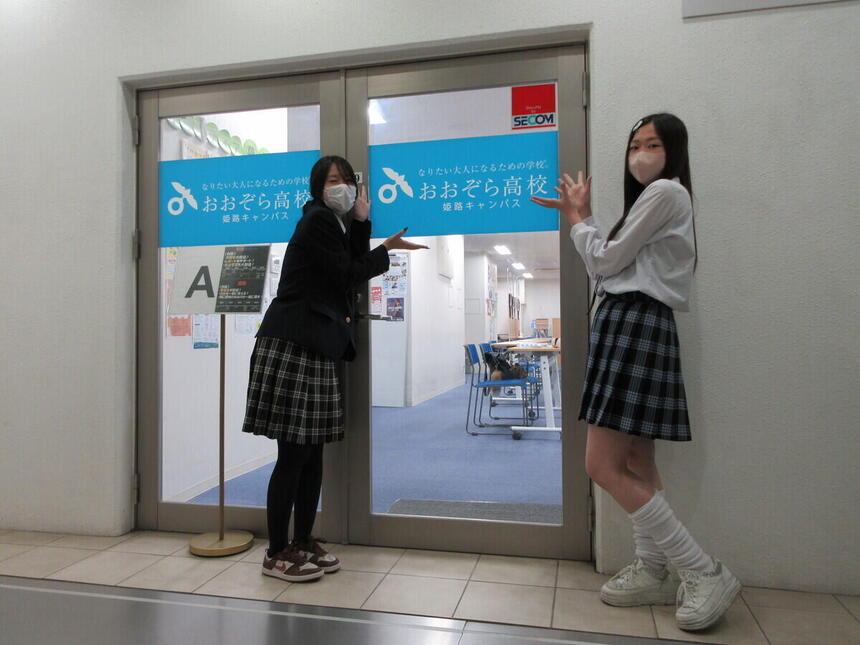 おおぞら高校 姫路キャンパスに在籍している女子生徒2名が教室の入口に立ち、扉を手のひらで指し示している様子を撮影した写真。