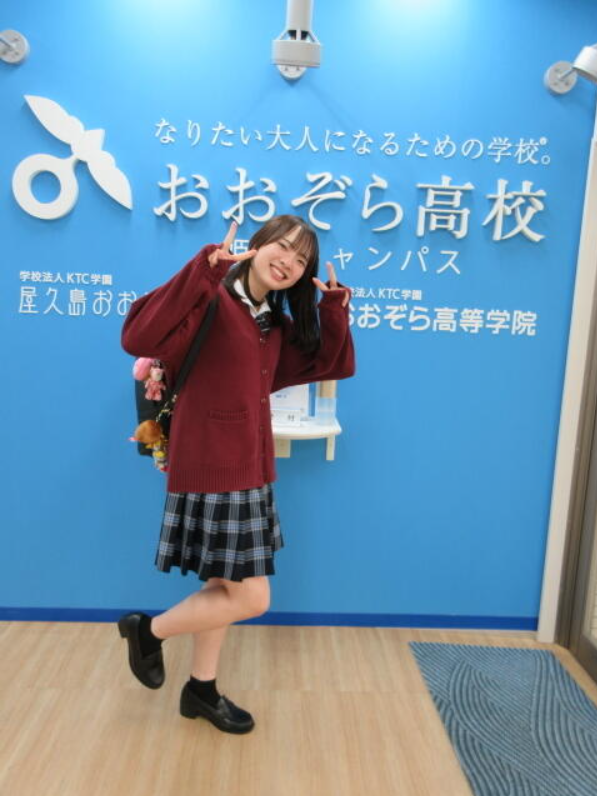 姫路キャンパスの看板の前でスクールバッグを背負ってピースする姫路キャンパスの女子生徒