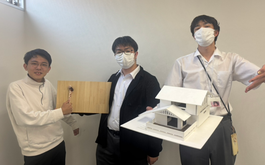 キャンパスで住環境デザインコースの生徒が、協力して製作した建築模型を持って集まっている写真