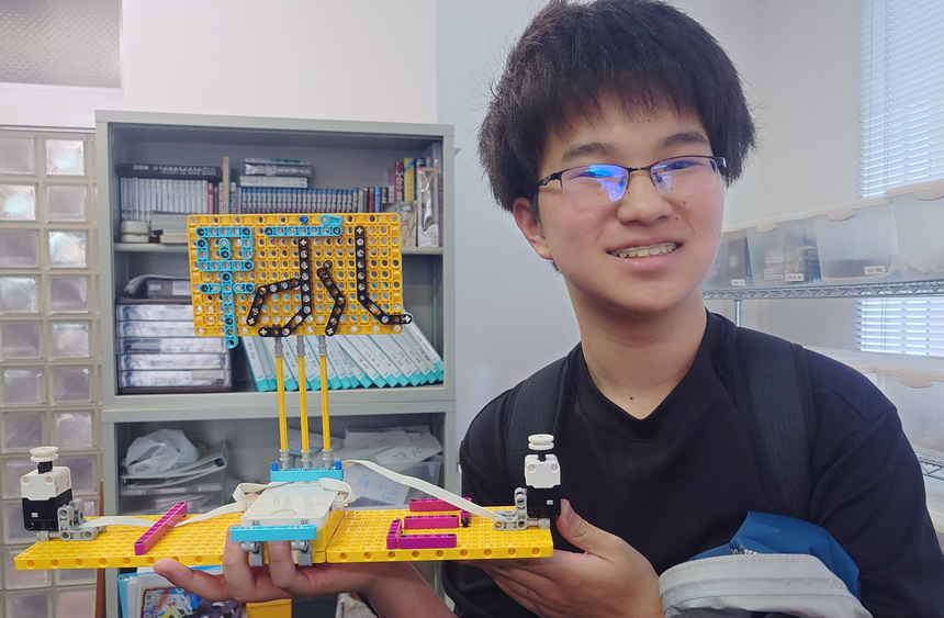 プログラミングの授業で、自作のオリジナルロボットを持ち笑顔で写真に写る生徒