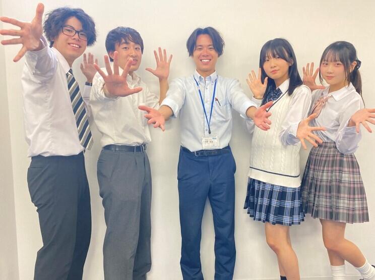 キャンパスの教室で在校生とコーチが笑顔でカメラに向かってポーズを決めている様子