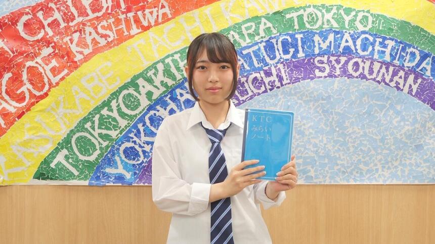 生徒が自分のKTCみらいノート®を持ってFESで使用した横断幕の前で撮った写真