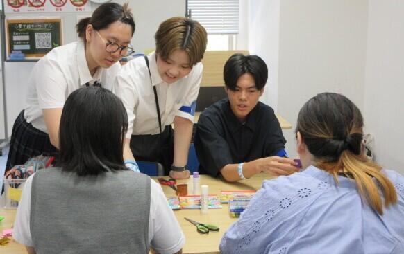 女子生徒2人と男子生徒1人が中学生と保護者に制作物の作り方を教えてている写真