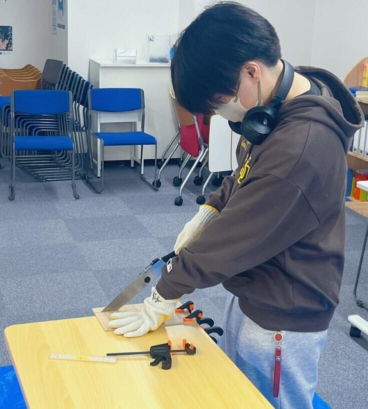 女子生徒が教室にて板をノコギリで切る作業をしている様子