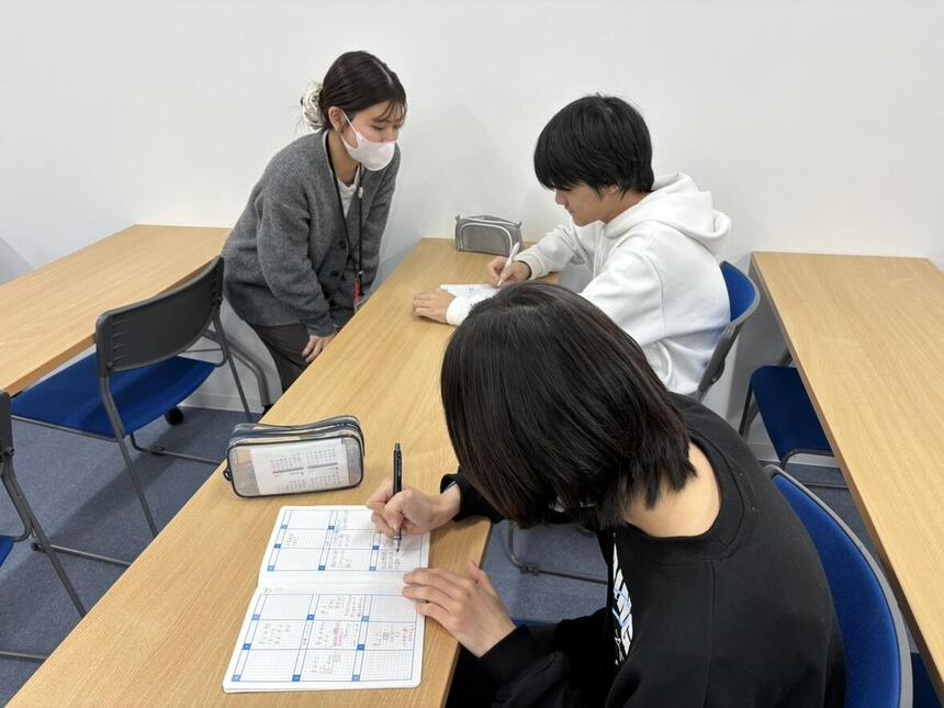 みらいノートに目標を書いている生徒２名と生徒と話しているコーチ