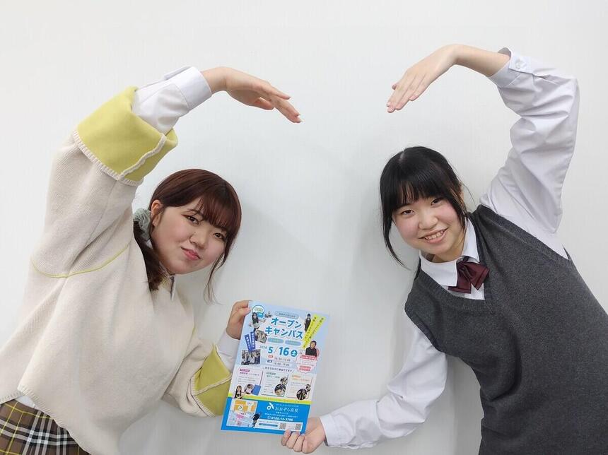2人の女子生徒がハートポーズをとって体験入学のチラシをご案内している写真。