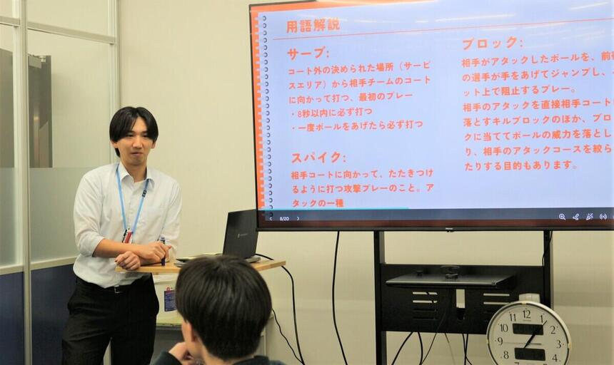 教室でバレーボールのルールを生徒たちに教えているコーチの写真