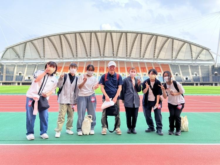 スタジアムを背景にボランティアのみなさんと並ぶ生徒