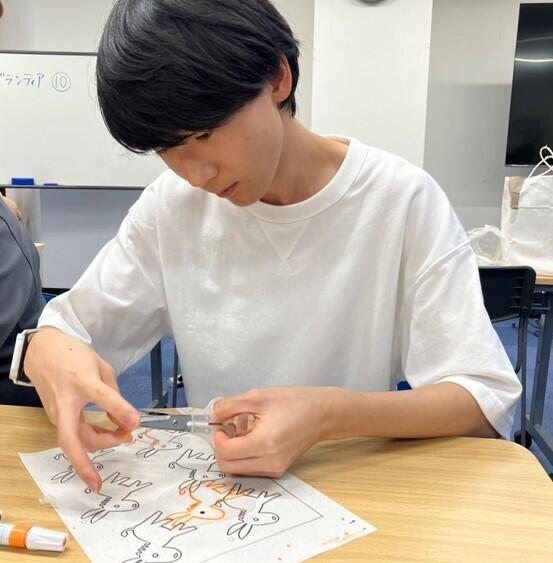 キーホルダーに使用するマスコットキャラクター「ロバ隊長」について、おおぞら高校熊本キャンパス男子生徒が型紙を使って作成している様子です。