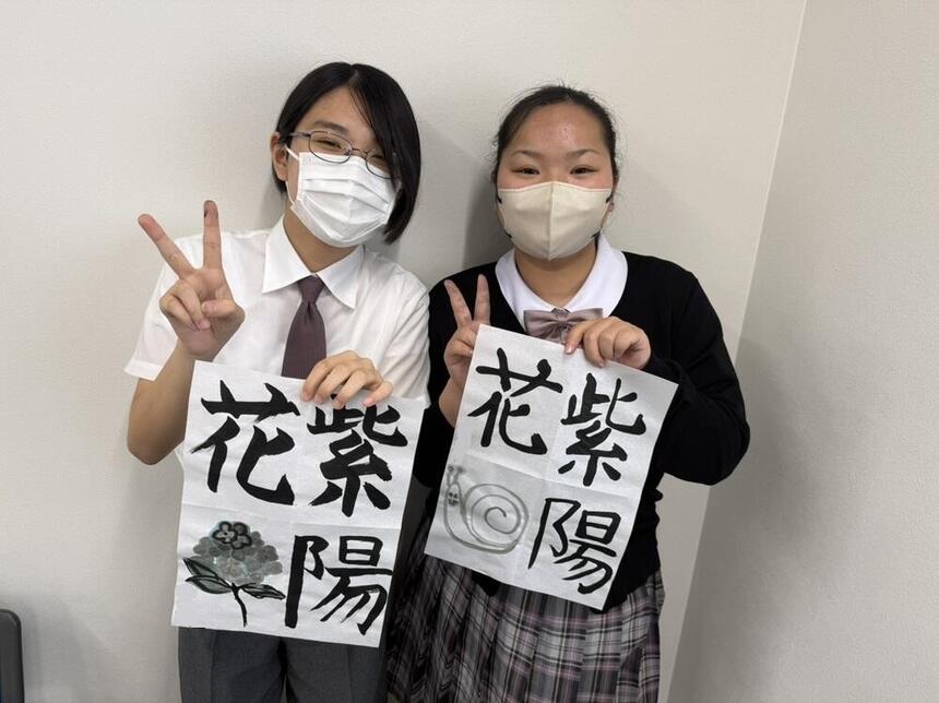 完成した自分の習字の作品を掲げて二人の女子生徒がピースしている写真