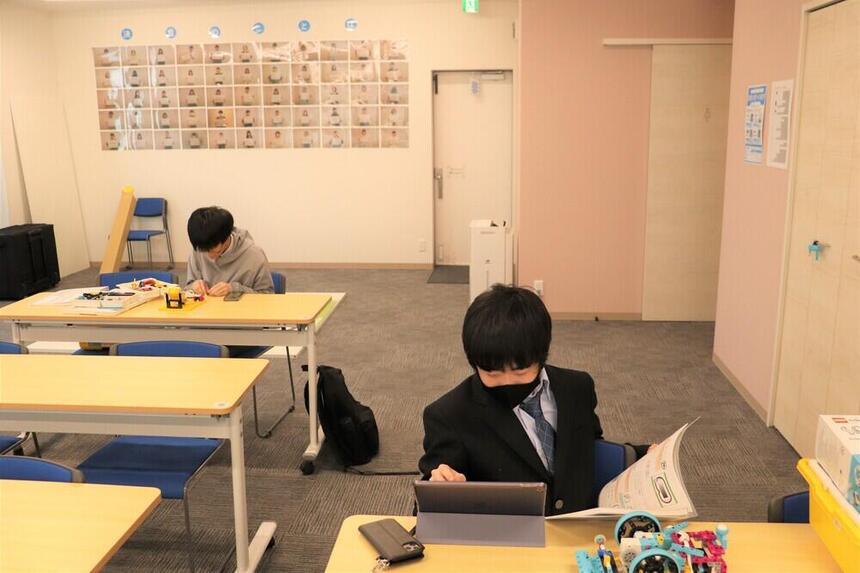 教室でプログラミングをしている男子生徒と教室でプログラミング用のマシンを組み立てている男子生徒の様子