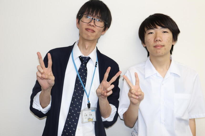 昼休みに教室の壁の前でピースサインをする男性コーチと昼休みに教室の壁の前でピースサインをする男子生徒