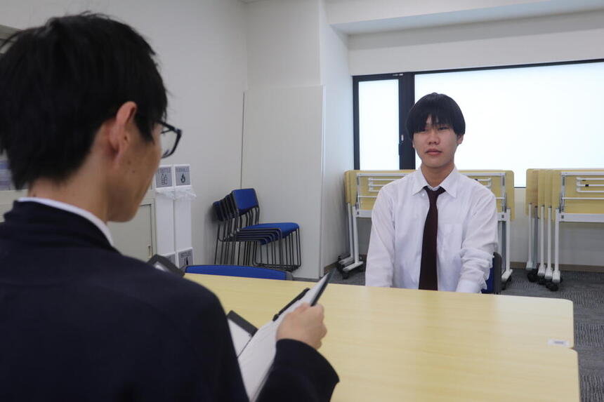 午前中に教室で面接練習をする男子生徒と午前中に教室で面接練習をする男性コーチ