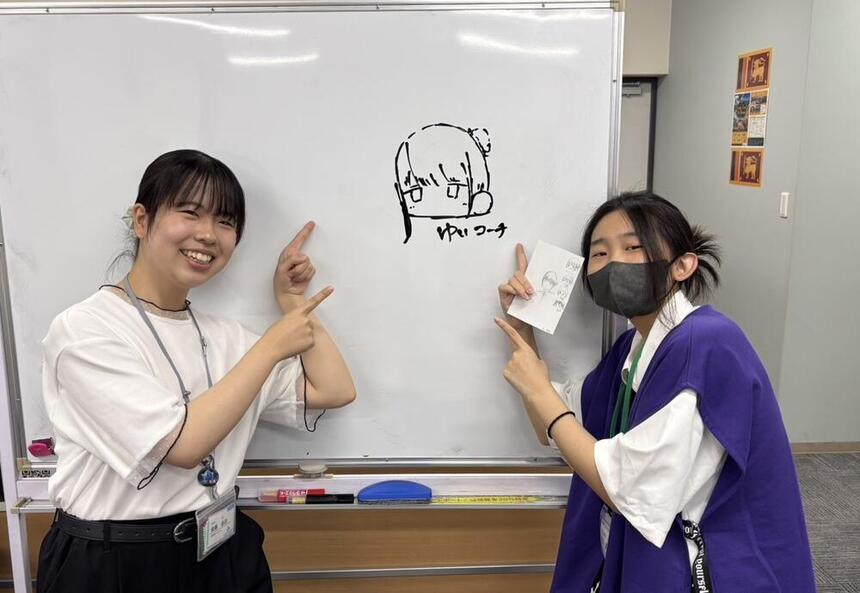 久留米キャンパスでコーチと生徒が描いたイラストの写真を撮影している様子。