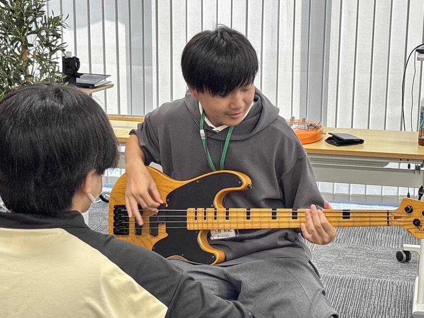 久留米キャンパスのオープンキャンパスで、在校生がお手伝い生徒として中学生・保護者を迎え、楽器体験ブースを実施している様子。