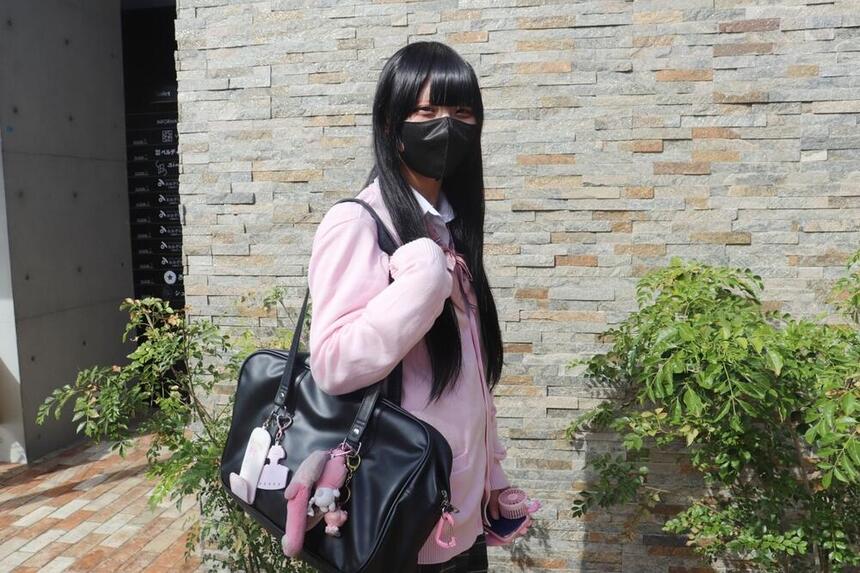 キャンパスの前で、ピンクの制服を着た女子生徒がポーズをとっている様子