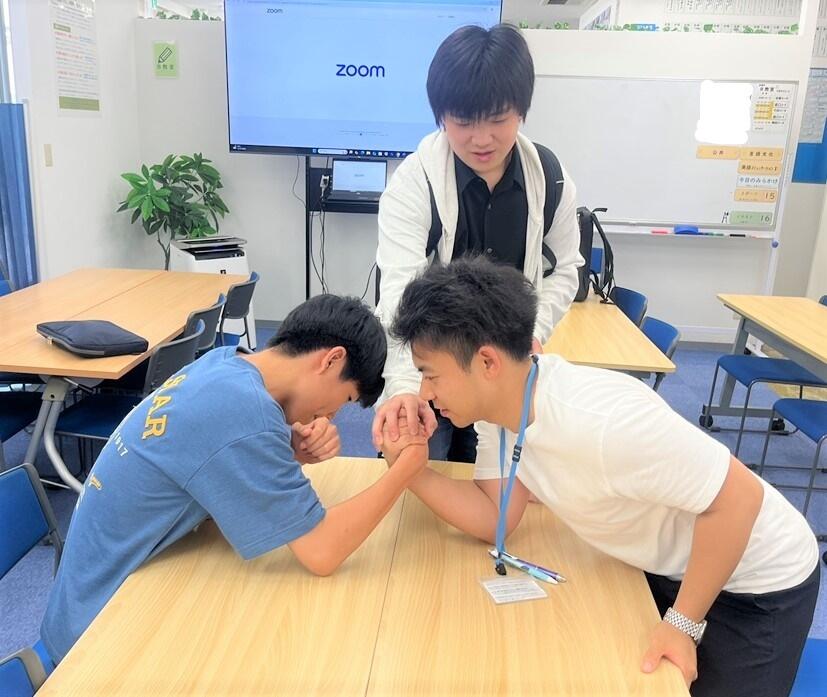 生徒と松野コーチの腕相撲。生徒とコーチの距離が近いのも特徴。