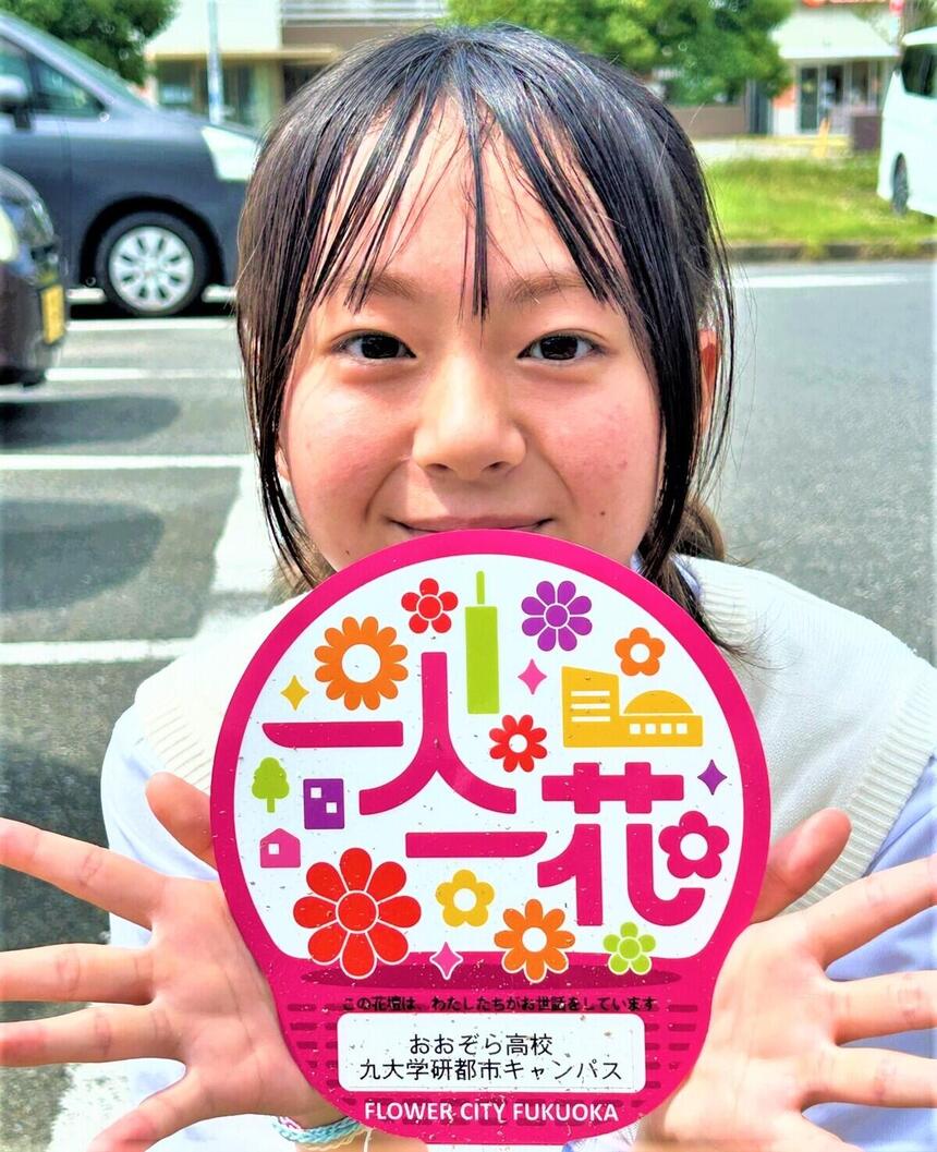 暑い中　福岡市『一人一花運動』の参加証明プレートを恥ずかしがって持つ　高校一年生女子