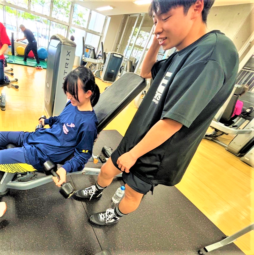 午後、キャンパス近くの公共施設で楽しみながら筋力トレーニングを行っている女子生徒と男子生徒