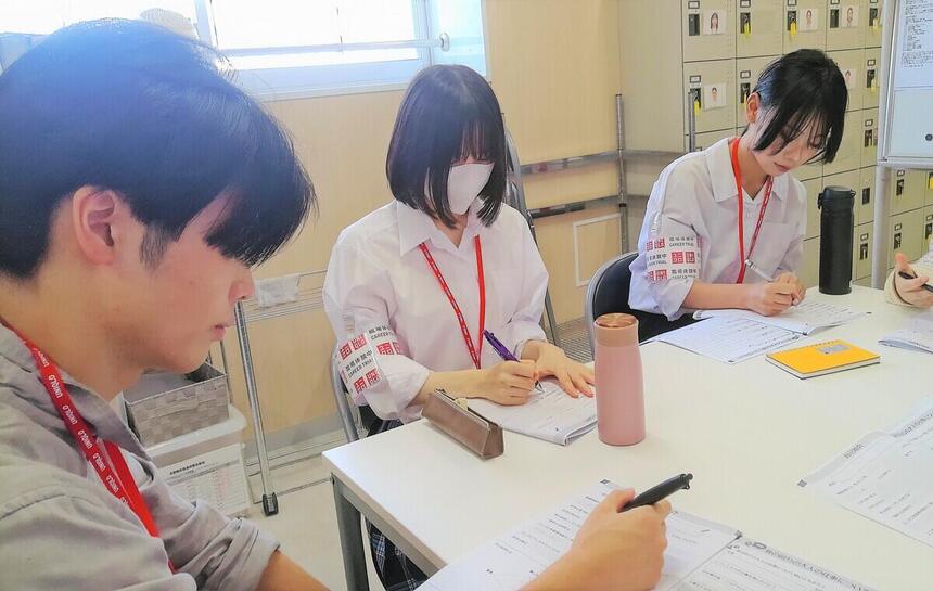 バックオフィスで担当者の方の話を聞きながらメモをしている生徒