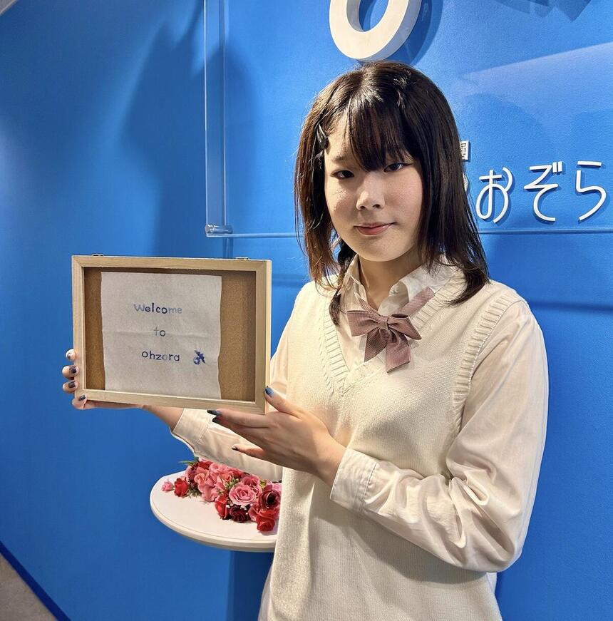 転校生インタビューを受けたOさんが刺繡した町田キャンパスのウエルカムボードを持っている写真