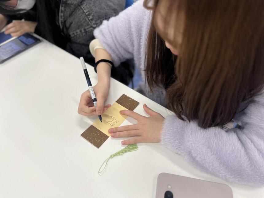 マンガイラストコースで生徒が栞に今年の目標を漢字一文字で書く様子。