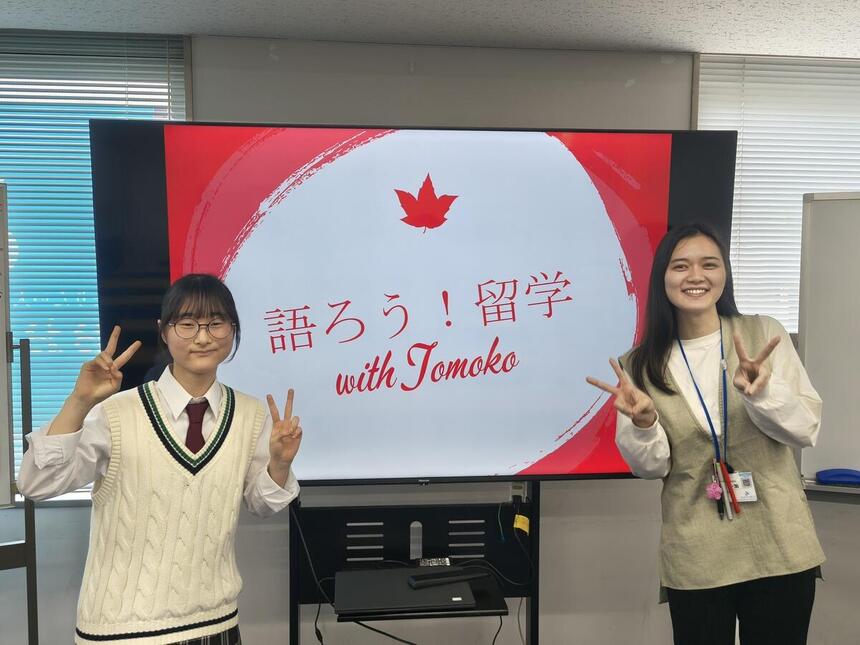 生徒がスライドを写したモニターの前でコーチと一緒に笑顔で立っている写真