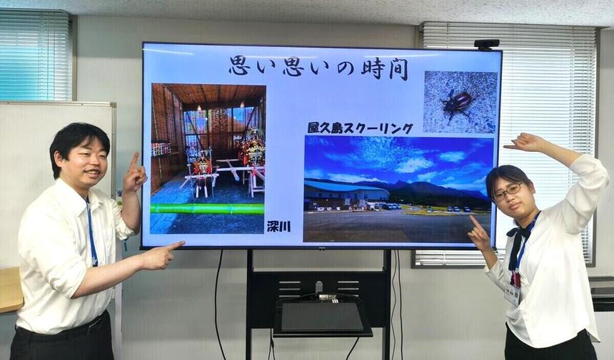 夏休みの思い出の写真を前に笑顔で2人のコーチが写る写真