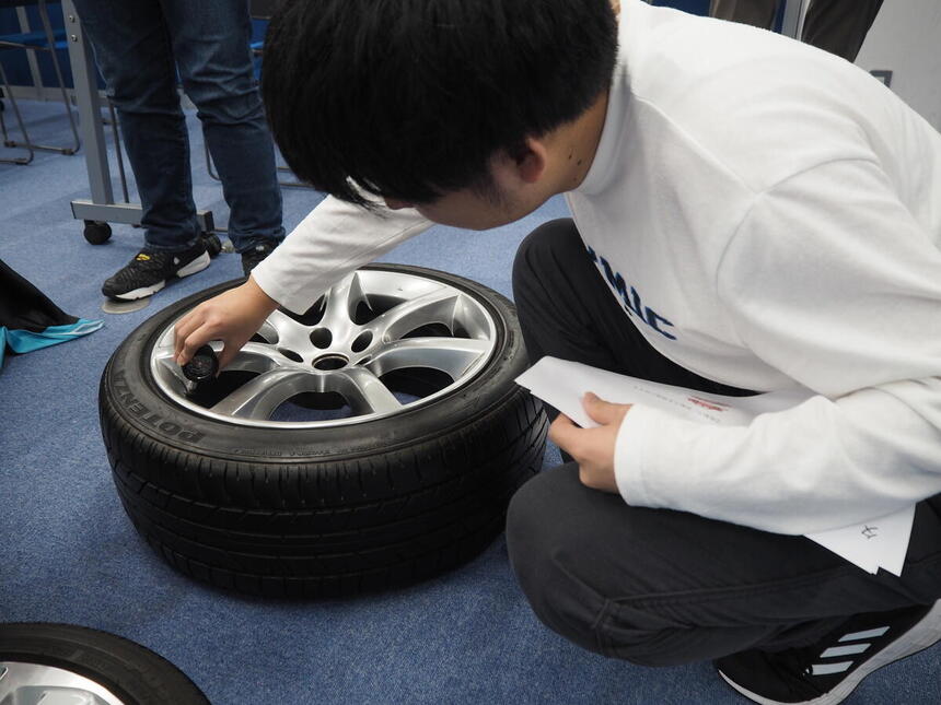 工具を使ってタイヤの空気圧を測定する生徒