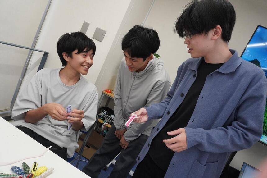 Kさんが参加生徒2名に笑顔でパラコードの編み方を教えている様子
