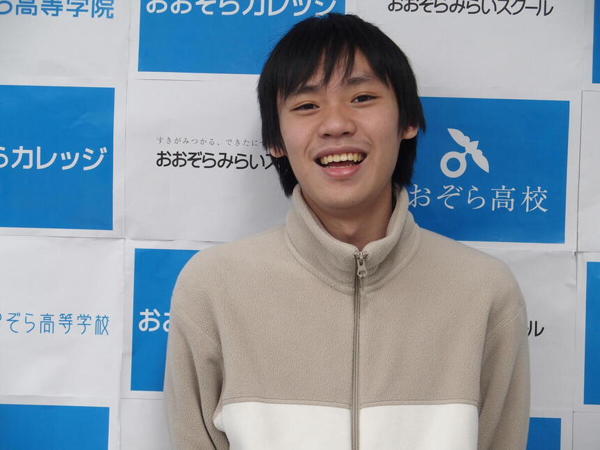 肌色の上着を着た笑顔の男の子　背景は印刷したおおぞら高校のグラフィック