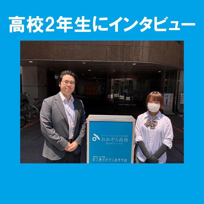 昼間　看板の横に移る　男性スタッフと女子生徒　前で腕を組んでいる。