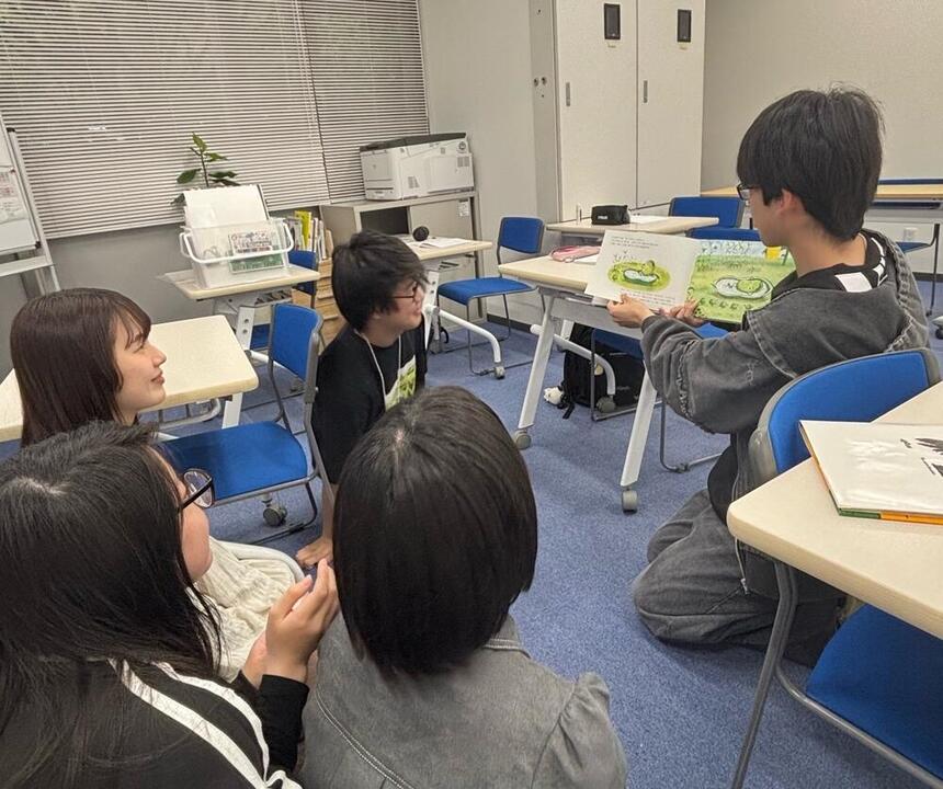 みらい学科™ 子ども・福祉コースの男子生徒が絵本を読み聞かせし、それを座って聞く同じコースの生徒