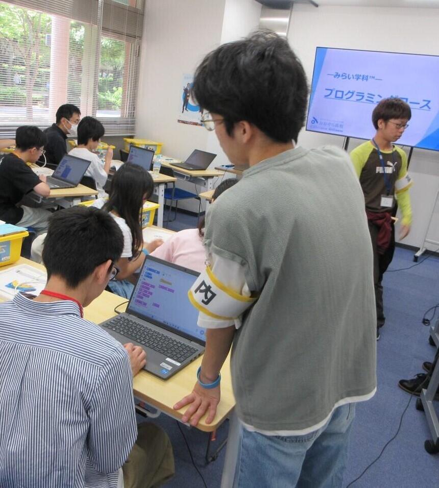 オープンキャンパスで在校生が中学生にプログラミングを教えている様子