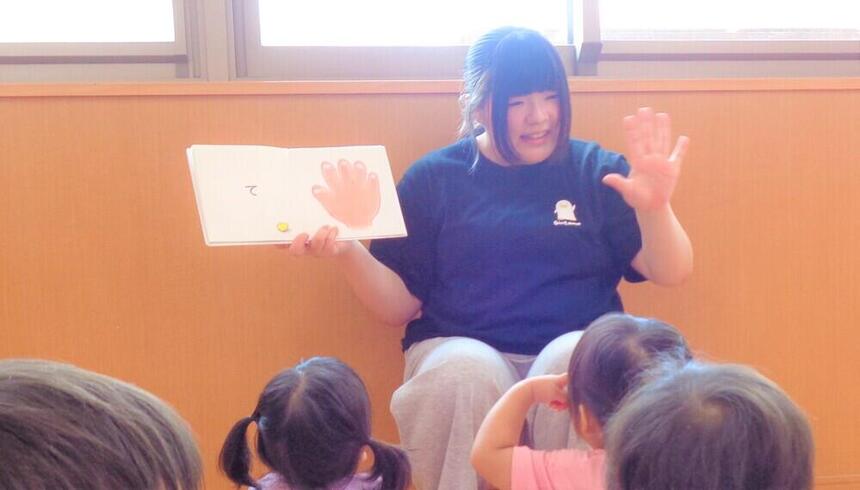 桜町こども園の園児の前で、絵本を見せながら読み聞かせをしている女子生徒1名