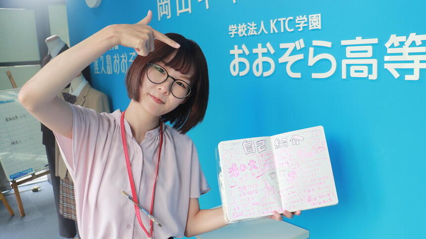 岡山キャンパス玄関口でポーズをしている清水コーチの写真です。
