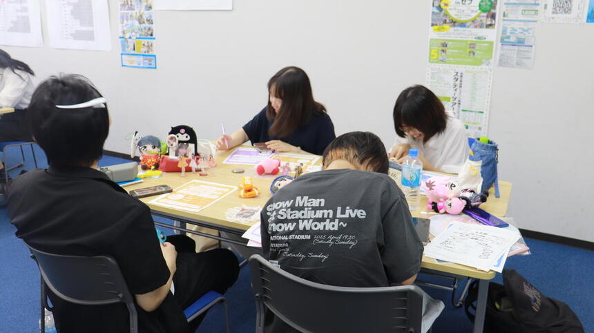 夏休みのある日、教室で生徒たちが推し活グッズを作成している様子です。
