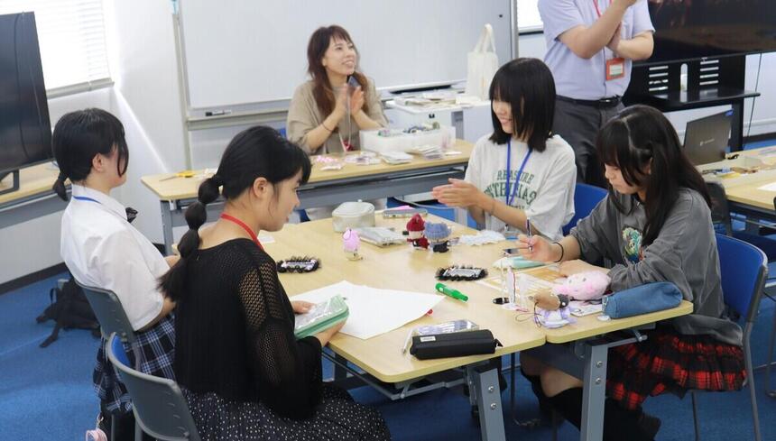岡山キャンパスの教室で、推しグッズ作成を楽しみながら笑顔を浮かべるコーチと生徒たちの写真